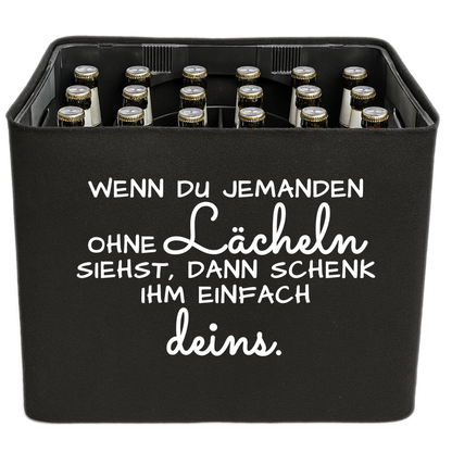 Schwarze KistenBlende mit weißem Spruch „Wenn du jemanden ohne Lächeln siehst, dann schenk ihm einfach deins.“ – Bier 24 × 0,33 l und Bier 20 × 0,5 l.