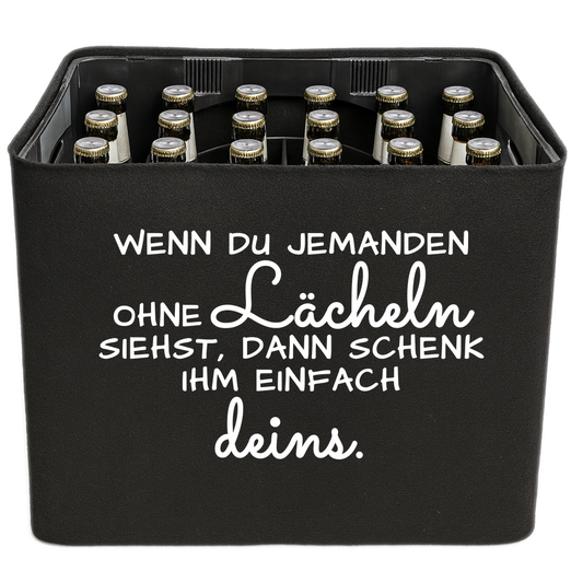 Schwarze KistenBlende mit weißem Spruch „Wenn du jemanden ohne Lächeln siehst, dann schenk ihm einfach deins.“ – Bier 24 × 0,33 l und Bier 20 × 0,5 l.
