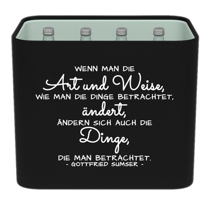 Schwarze KistenBlende mit weißem Spruch „Wenn man die Art und Weise, wie man die Dinge betrachtet, ändert, ändern sich auch die Dinge, die man betrachtet. — Gottfried Sumser“ – Wasser Glas.