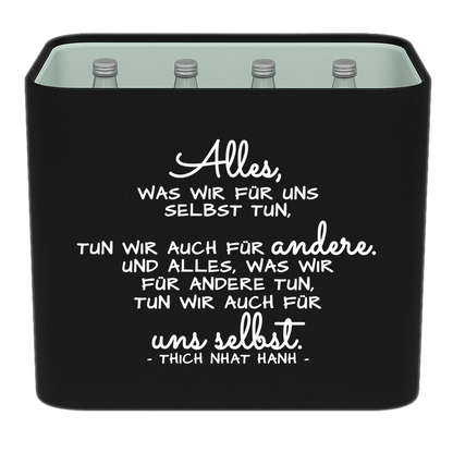 Schwarze KistenBlende mit weißem Spruch „Alles, was wir für uns selbst tun, tun wir auch für andere. Und alles, was wir für andere tun, tun wir auch für uns selbst. — Thich Nhat Hanh“ – Wasser Glas.